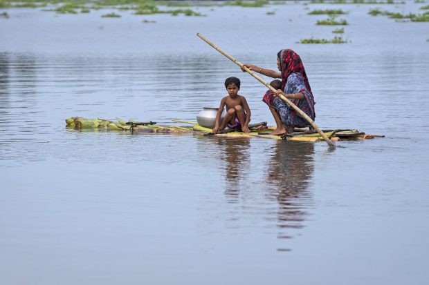 A woman with children rows a raft made from banana trees toward a safer area from the flooded village of Tarabari, in Assam. (AP Photo)