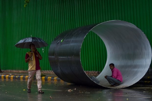 A man sits inside a pipe to avoid the rain in New Delhi on Saturday. (PTI)