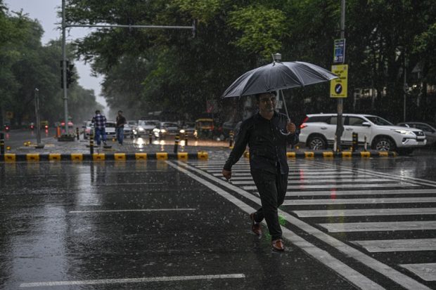 A man crosses a road during the rain on Saturday. (PTI)