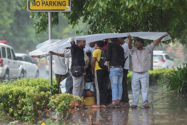 Commuters user a plastic sheet to protect themselves from the rain in New Delhi on Saturday. (PTI)