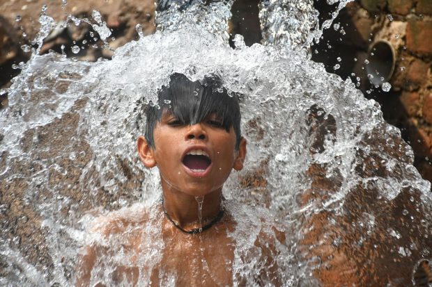 A boy takes bath under a water-pipeline on a hot summer afternoon, in New Delhi. (PTI Photo)