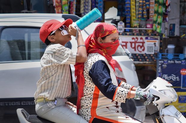 A student drinks water while riding a two-wheeler to quench his thirst on a hot summer afternoon, in Bikaner. (PTI Photo)