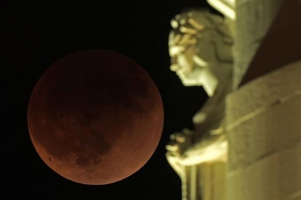 A lunar eclipse covers the moon as it rises beyond a statue atop the Liberty Memorial tower at the National World War I Museum in Kansas City. (AP Photo)