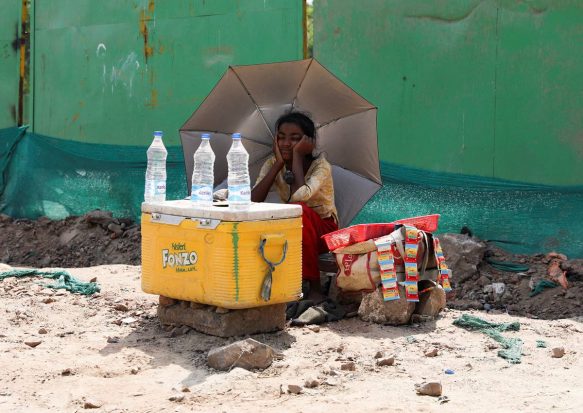 A girl selling water uses an umbrella to protect herself from the sun as she waits for customers on a hot summer day, in New Delhi. (Reuters image)