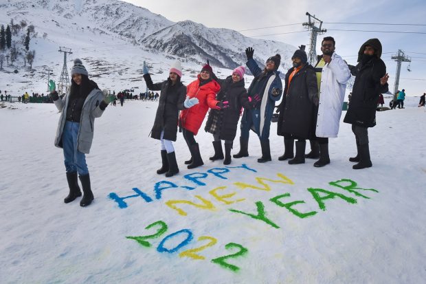 Tourists pose for photographs as they stand near a message 'Happy New Year 2022' painted on snow near a ski resort in Gulmarg (PTI Photo)